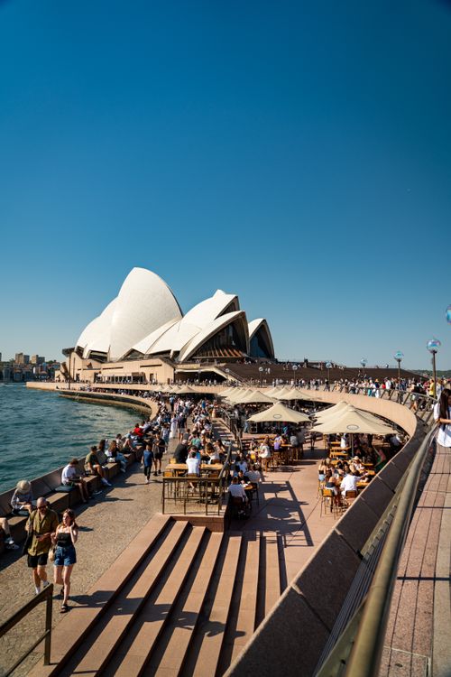 Free Vibrant scene of the Sydney Opera House with people enjoying the sunny day on the bustling promenade. Stock Photo