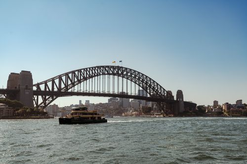 Free Cityscape featuring the iconic Sydney Harbour Bridge and ferry crossing the water. Stock Photo