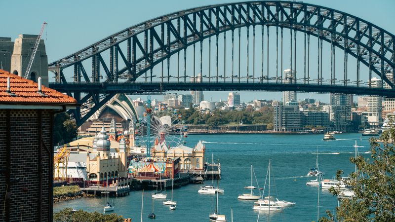 A vibrant view of Sydney Harbour Bridge with Luna Park and sailboats highlighting the iconic skyline.