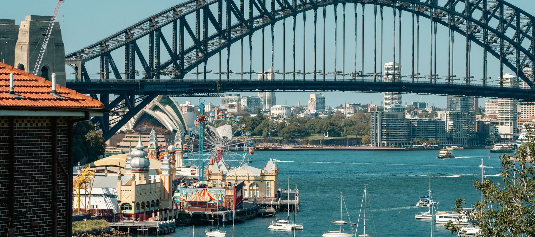 A vibrant view of Sydney Harbour Bridge with Luna Park and sailboats highlighting the iconic skyline.