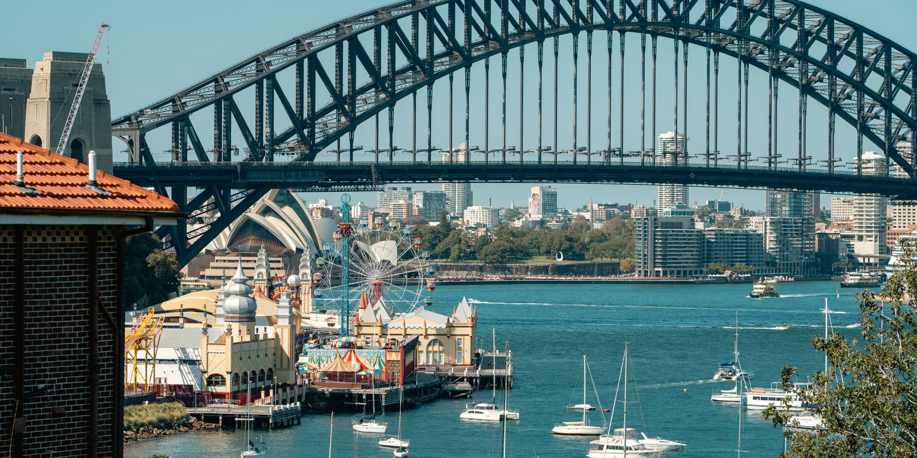 A vibrant view of Sydney Harbour Bridge with Luna Park and sailboats highlighting the iconic skyline.