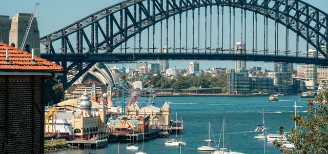A vibrant view of Sydney Harbour Bridge with Luna Park and sailboats highlighting the iconic skyline.
