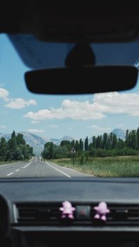 View from a car interior driving through a scenic countryside with mountains ahead.