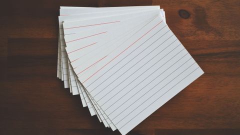 High-angle view of blank index cards arranged neatly on a wooden desk, ideal for education and organization concepts.