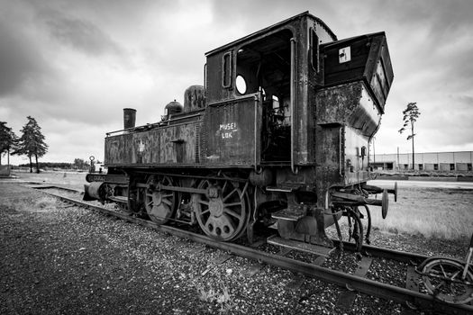 Black and white image of an abandoned rusty locomotive on railway tracks.