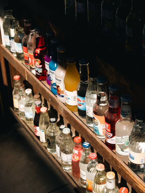 Free An array of colorful bottled beverages illuminated by sunlight on wooden shelves. Stock Photo