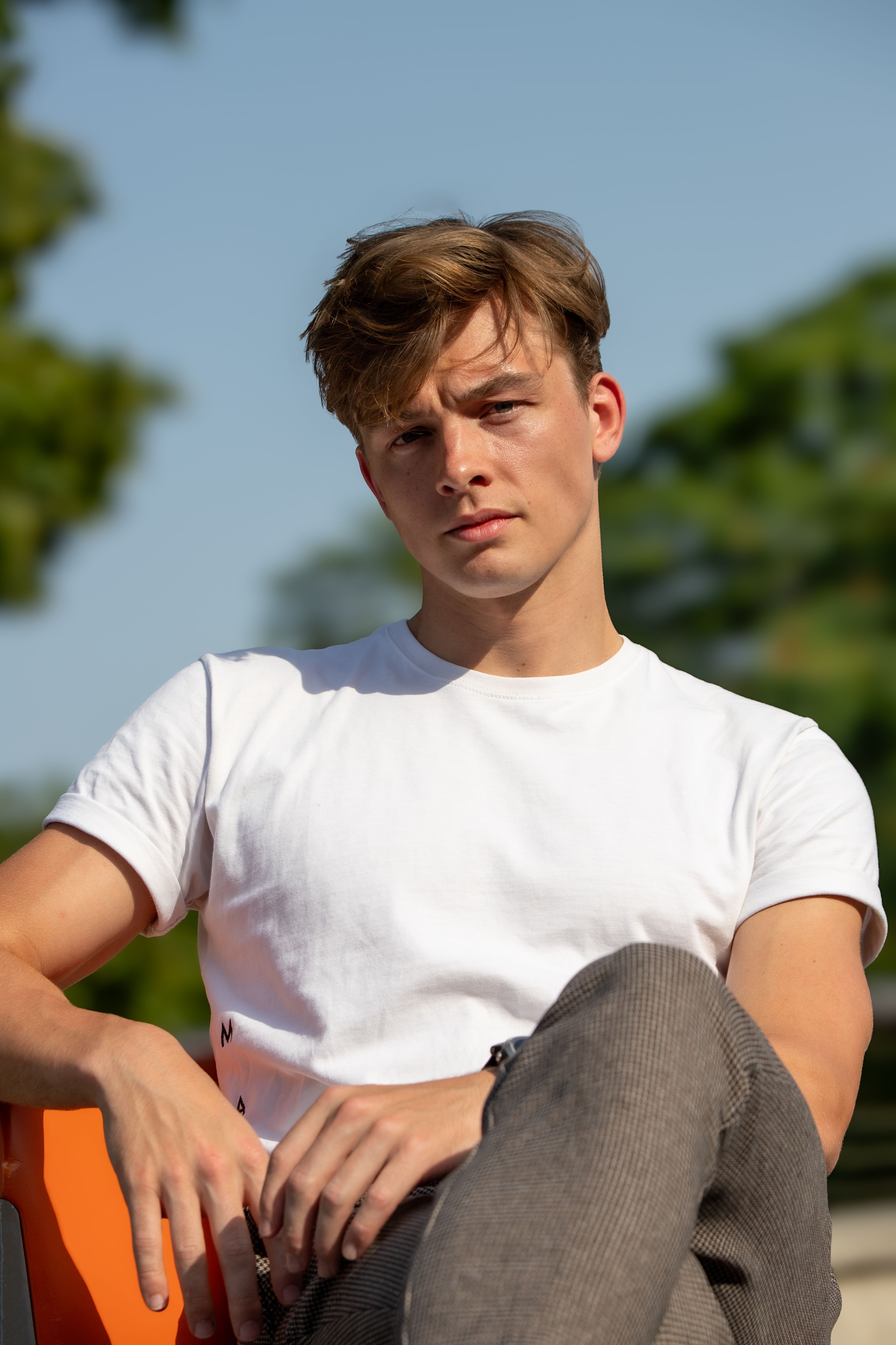 Casual portrait of a young man in a white t-shirt, seated outdoors in a Berlin park on a sunny day.