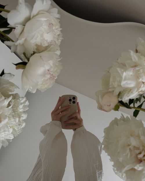 Free A serene reflection of a person holding a smartphone surrounded by white flowers in a mirror. Stock Photo