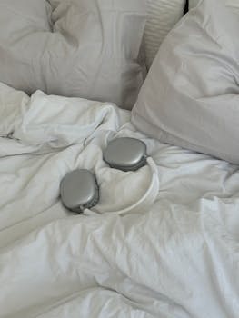 Cozy bedroom scene with luxury headphones on a bed with soft white pillows.