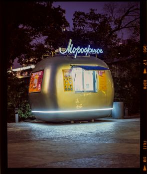 Illuminated ice cream kiosk with modern design in a nighttime urban setting.