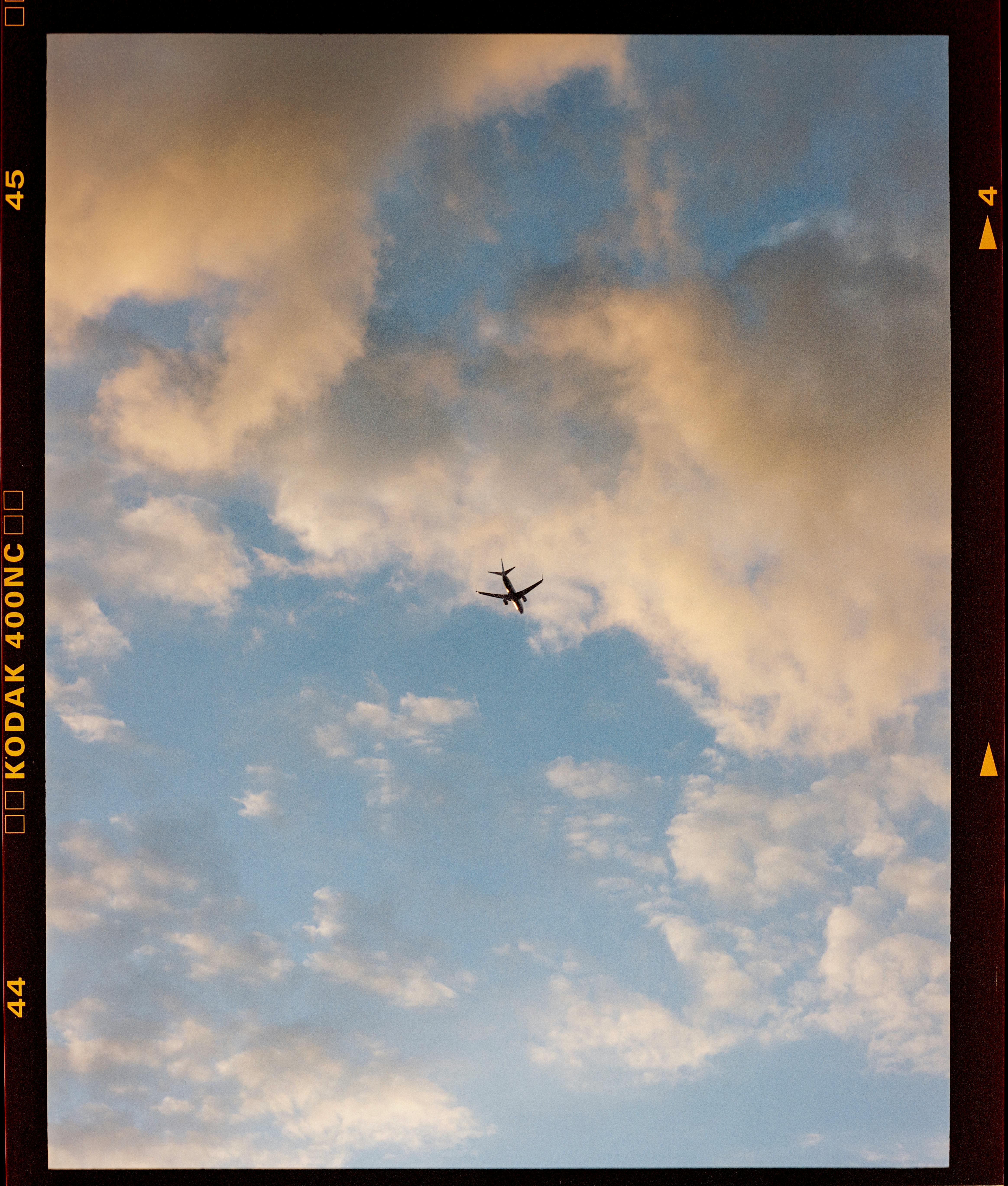 A lone airplane flies through a vibrant, cloud-filled sky, captured in a vertical shot.