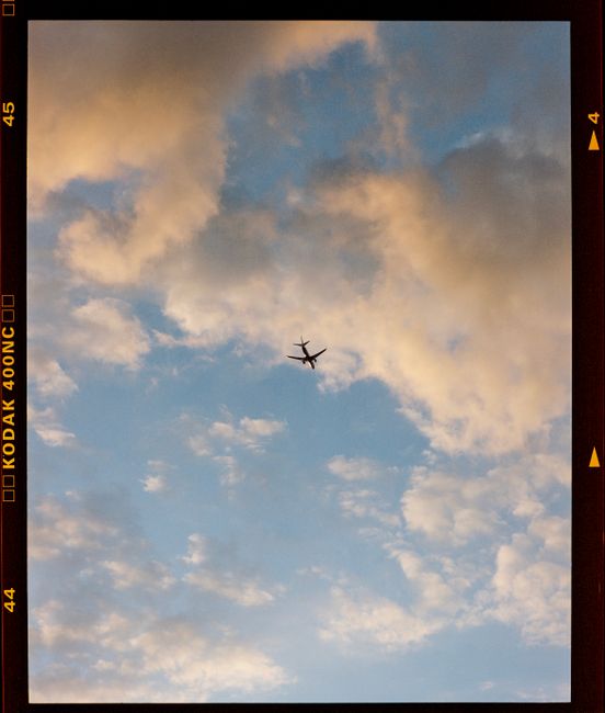 A lone airplane flies through a vibrant, cloud-filled sky, captured in a vertical shot.