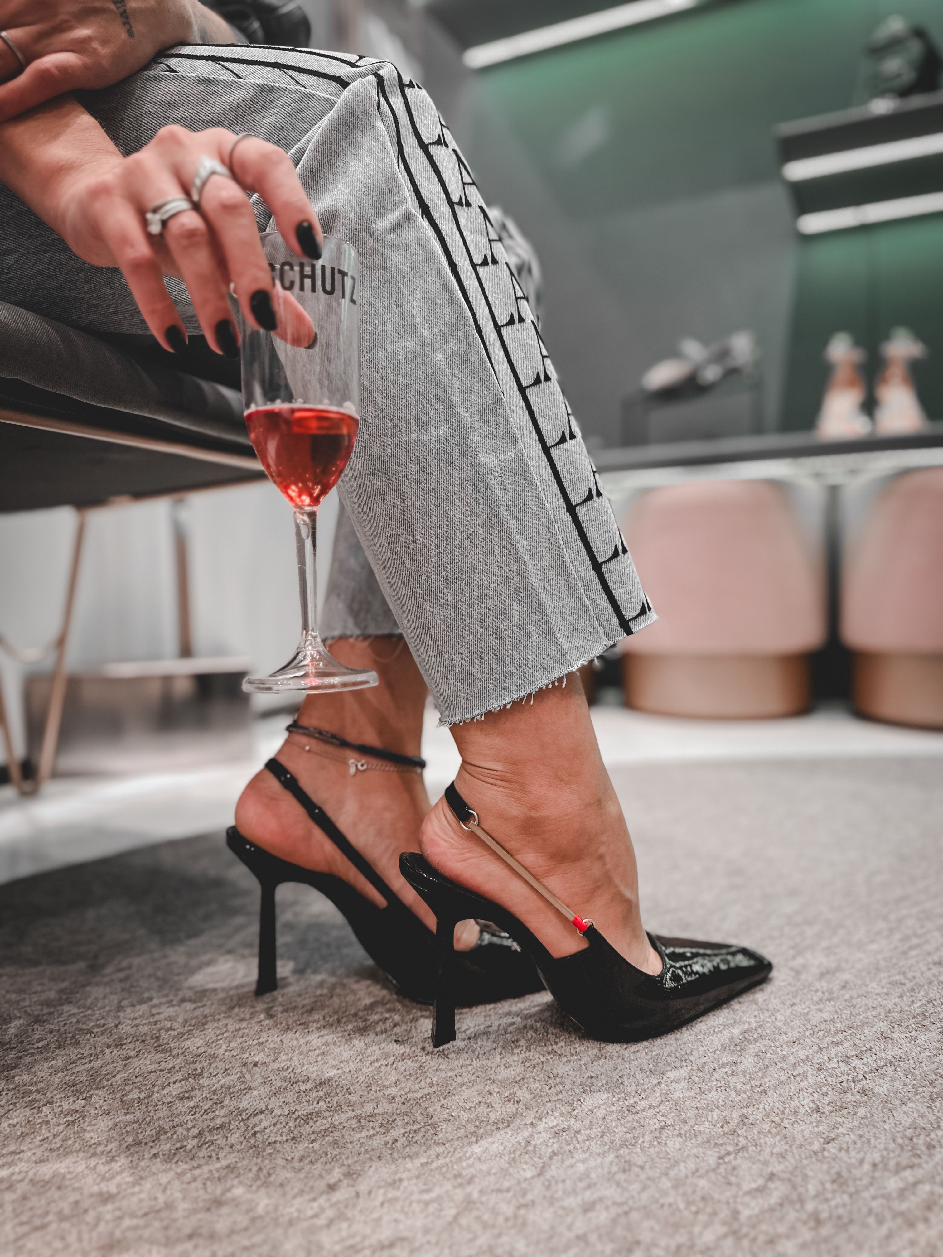 Mulher estilosa em saltos pretos segurando um copo de vinho dentro de casa, mostrando moda moderna.
