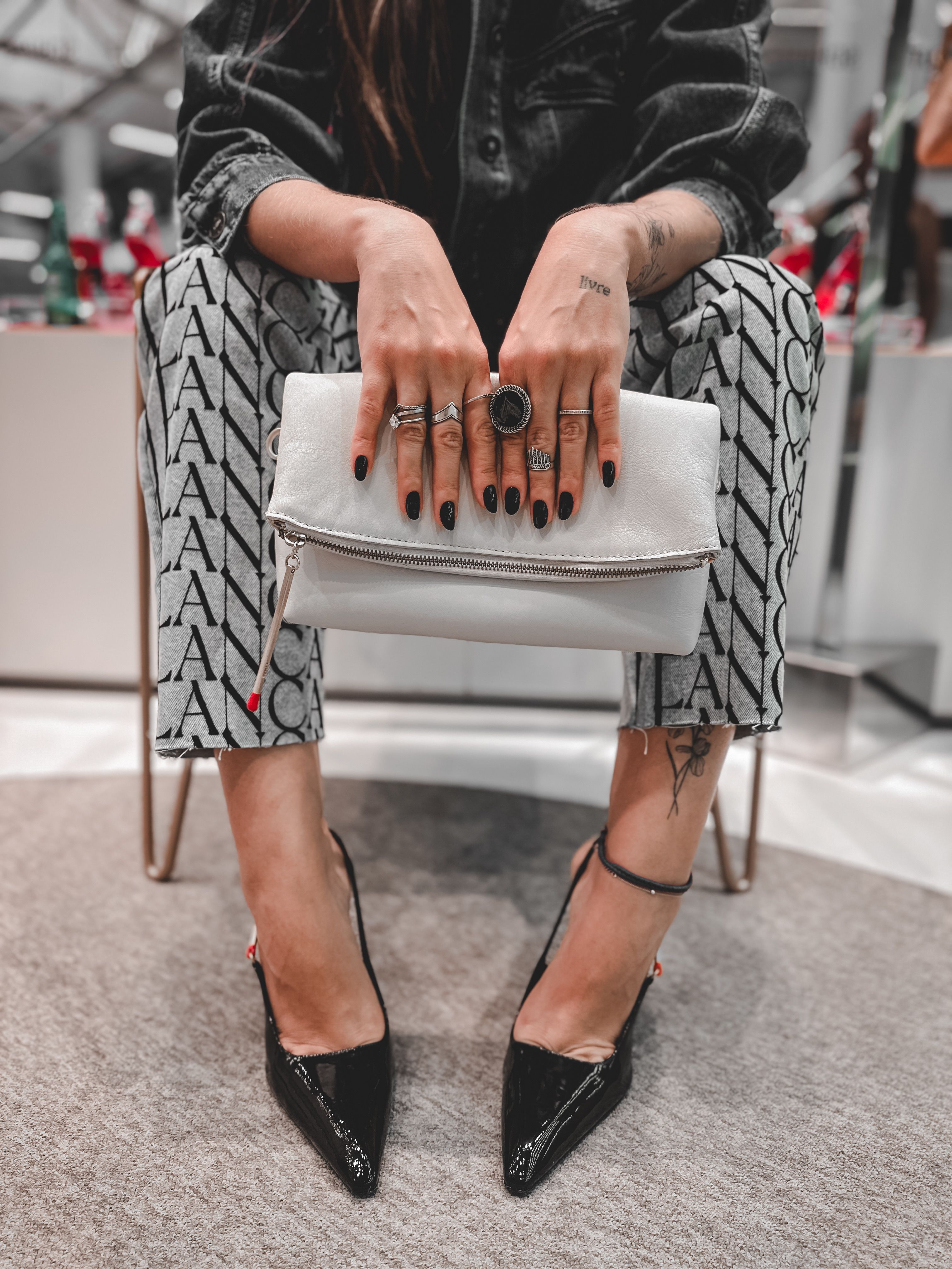 Mulher fashionista sentada elegantemente em uma cadeira, exibindo seu salto alto preto e clutch branca com elegância.