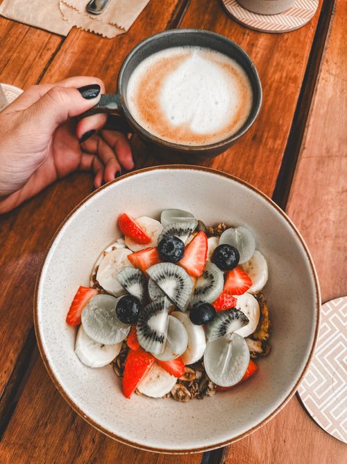 Free A vibrant breakfast bowl with fresh fruits and a hot cup of coffee on a wooden table. Stock Photo