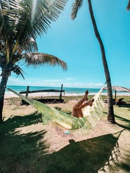 Woman relaxing in a hammock under palm trees by the tropical seaside.