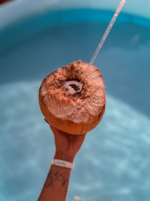 Free Hand holding a fresh coconut with straw by a clear pool, ideal for summer vacation themes. Stock Photo