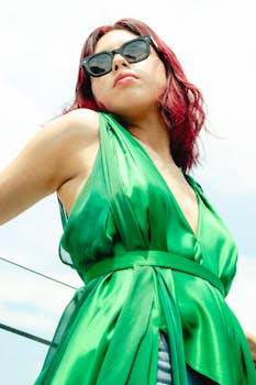 Confident woman poses in a vibrant green dress and sunglasses, embracing summer fashion outdoors.