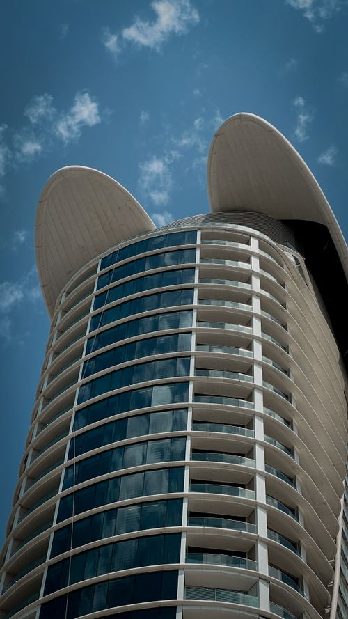Free Discover this striking modern skyscraper with curved lines under a blue sky, ideal for travel and architecture themes. Stock Photo
