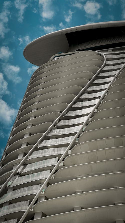 Free High-rise building with unique curved architecture set against a cloudy blue sky. Stock Photo