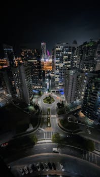 Bright city lights and skyscrapers captured from above at night in a bustling urban area.