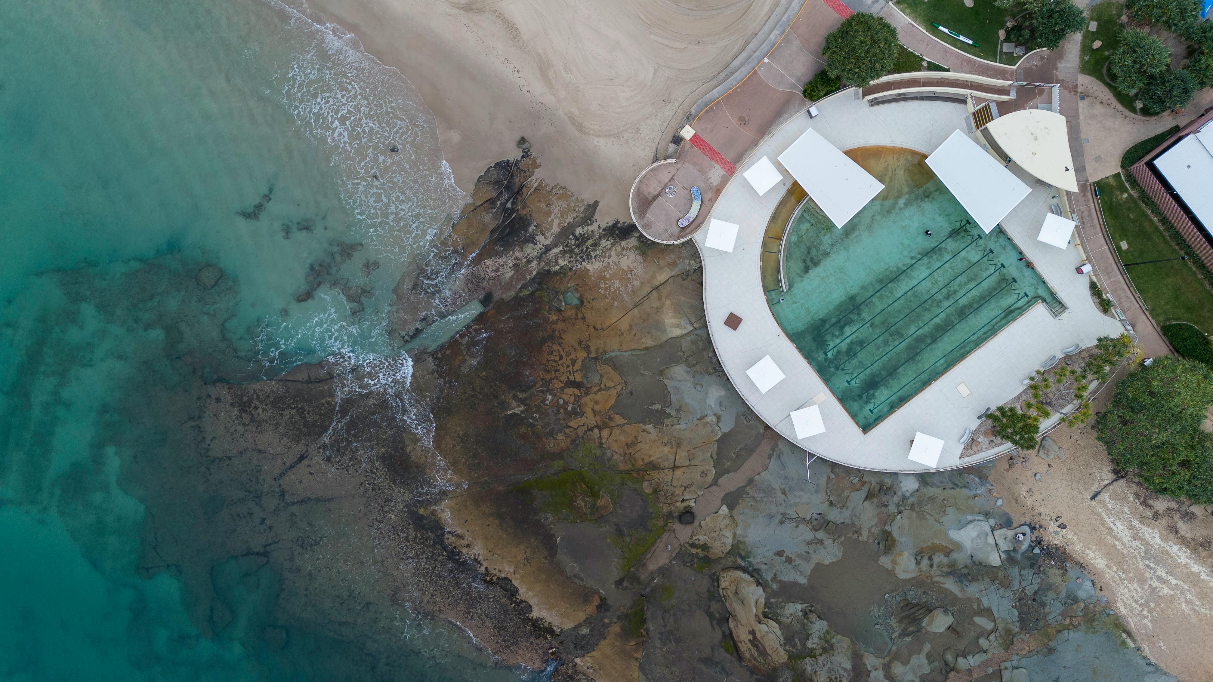 A stunning aerial view of a swimming pool by the rocky shoreline in Caloundra, Australia.