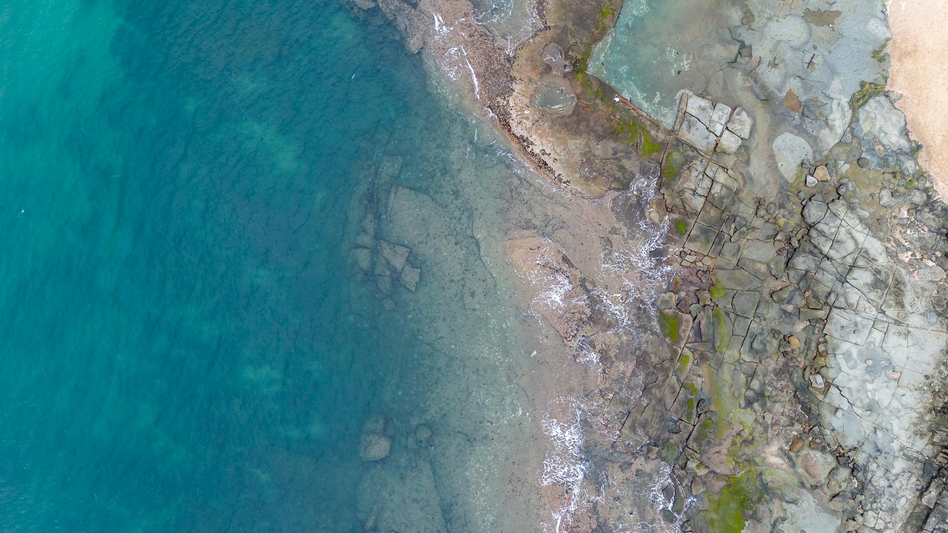 Aerial shot of Caloundra coastline in Queensland, featuring turquoise water and rocky shores.