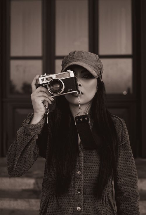 Free A fashionable woman in a cap taking a photo with a vintage camera. Stock Photo