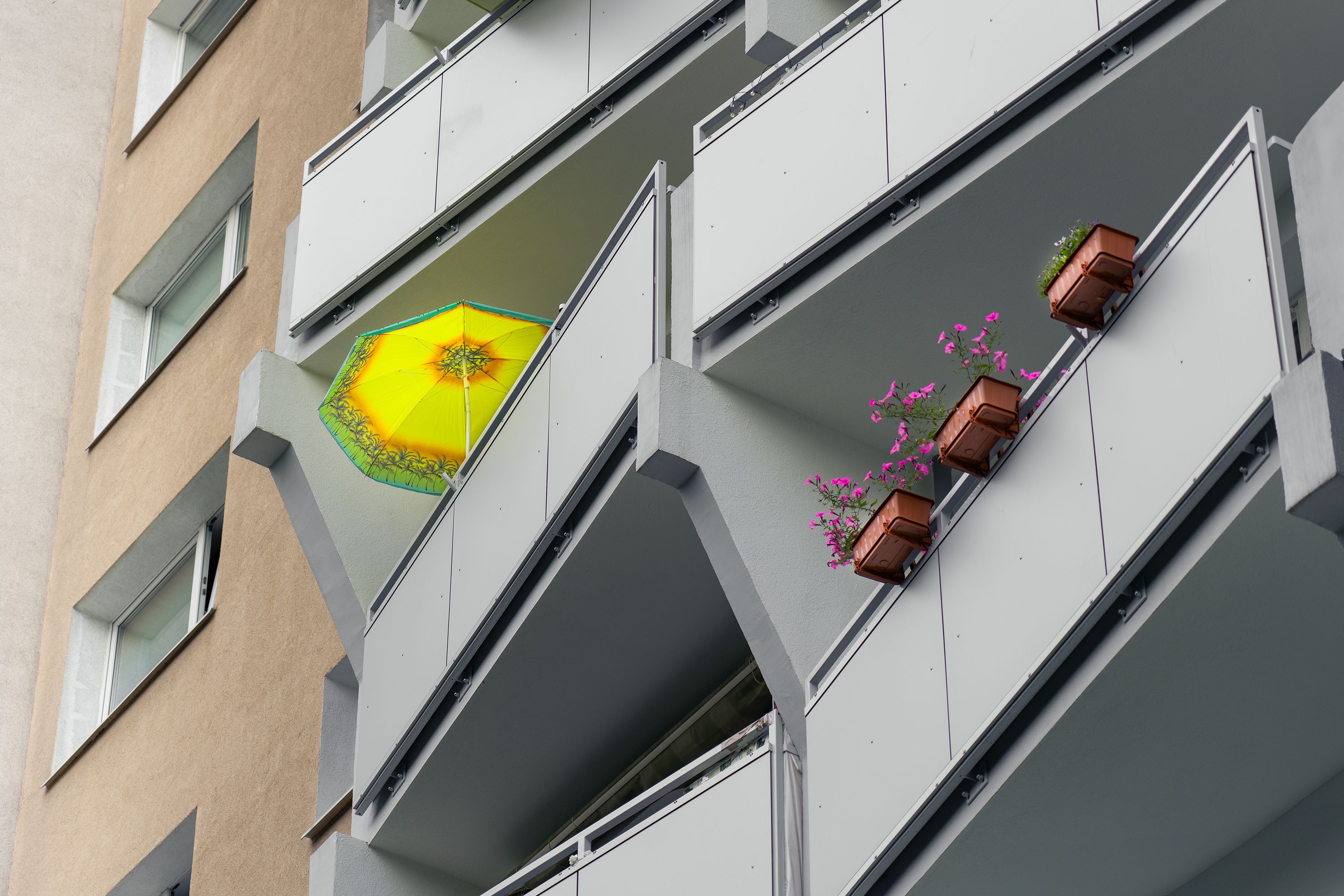 Free Contemporary apartment balcony with vibrant yellow umbrella and flower pots, showcasing urban elegance. Stock Photo
