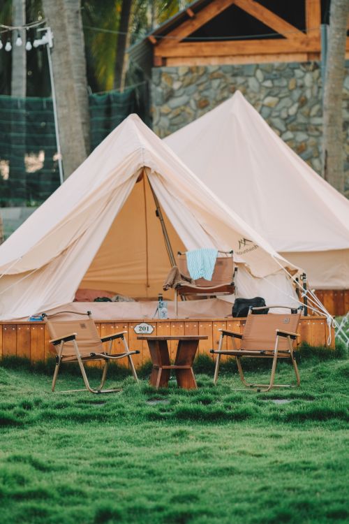 Free A serene outdoor camping scene featuring a tent with chairs on lush grass. Stock Photo