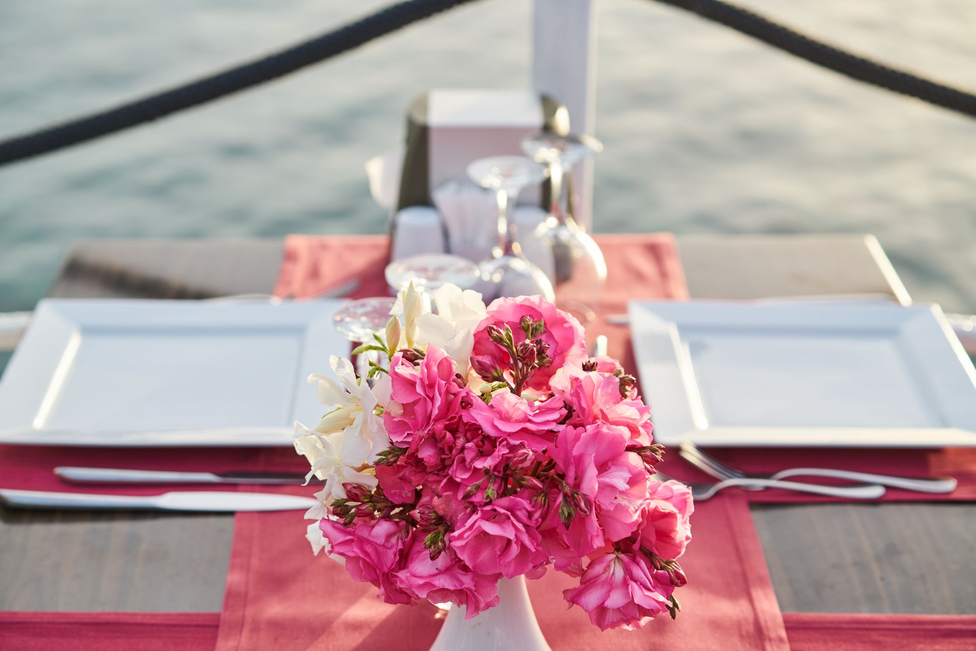 A beautifully set outdoor table with pink and white flower arrangement against a blurred sea backgro