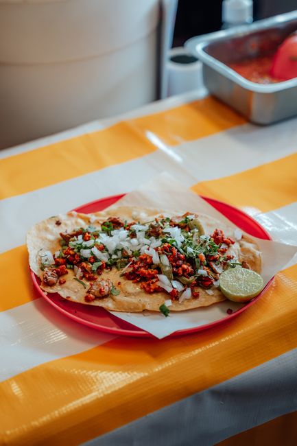 Crumbled browned chorizo piled on warm corn tortillas with diced white onion, chopped cilantro, and lime wedges on a dark plate.