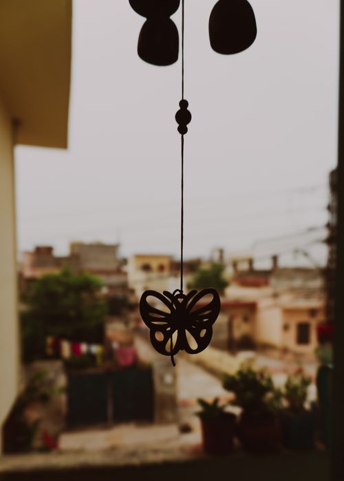 Free Silhouette of hanging butterfly decoration against a blurred urban townscape background. Stock Photo