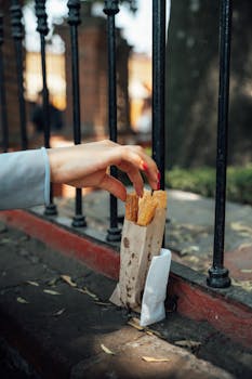 A hand picks churros from a paper bag by a wrought iron fence in Mexico City.