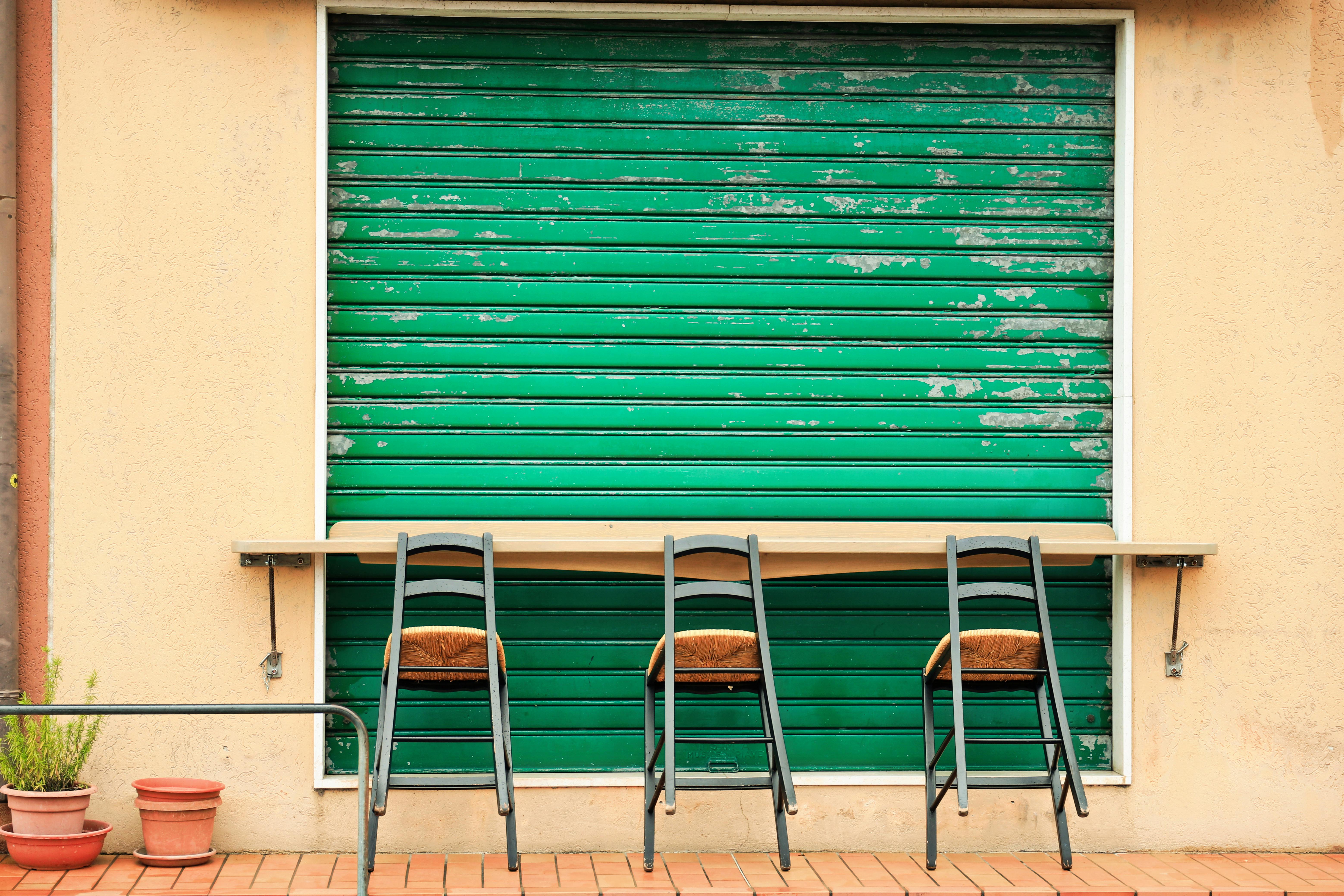 Three chairs lined up against a vibrant green shutter in an urban setting. Perfect for street photography themes.