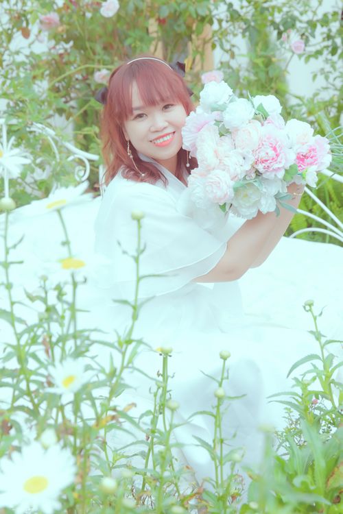 Free Asian woman in wedding dress smiling with a bouquet in a serene garden setting, embodying wedding joy. Stock Photo