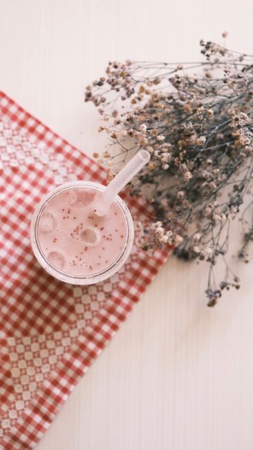 Cách Nấu Sữa Hạt Macca Thơm Béo Mịn, Không Bị Lợn Cợn 4 Top view of a refreshing strawberry smoothie with ice accompanied by dried flowers on a red checkered cloth.