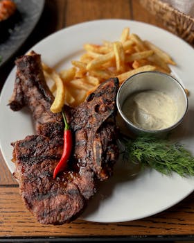 Savory grilled pork chop served with crispy fries and creamy sauce on a plate.