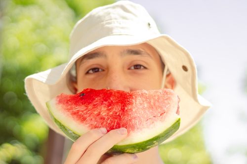 Free Young boy in a hat enjoying a fresh slice of watermelon on a sunny day outdoors. Stock Photo