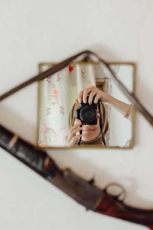Free Creative self-portrait reflection in a mirror, featuring a woman in a hijab holding a camera. Stock Photo