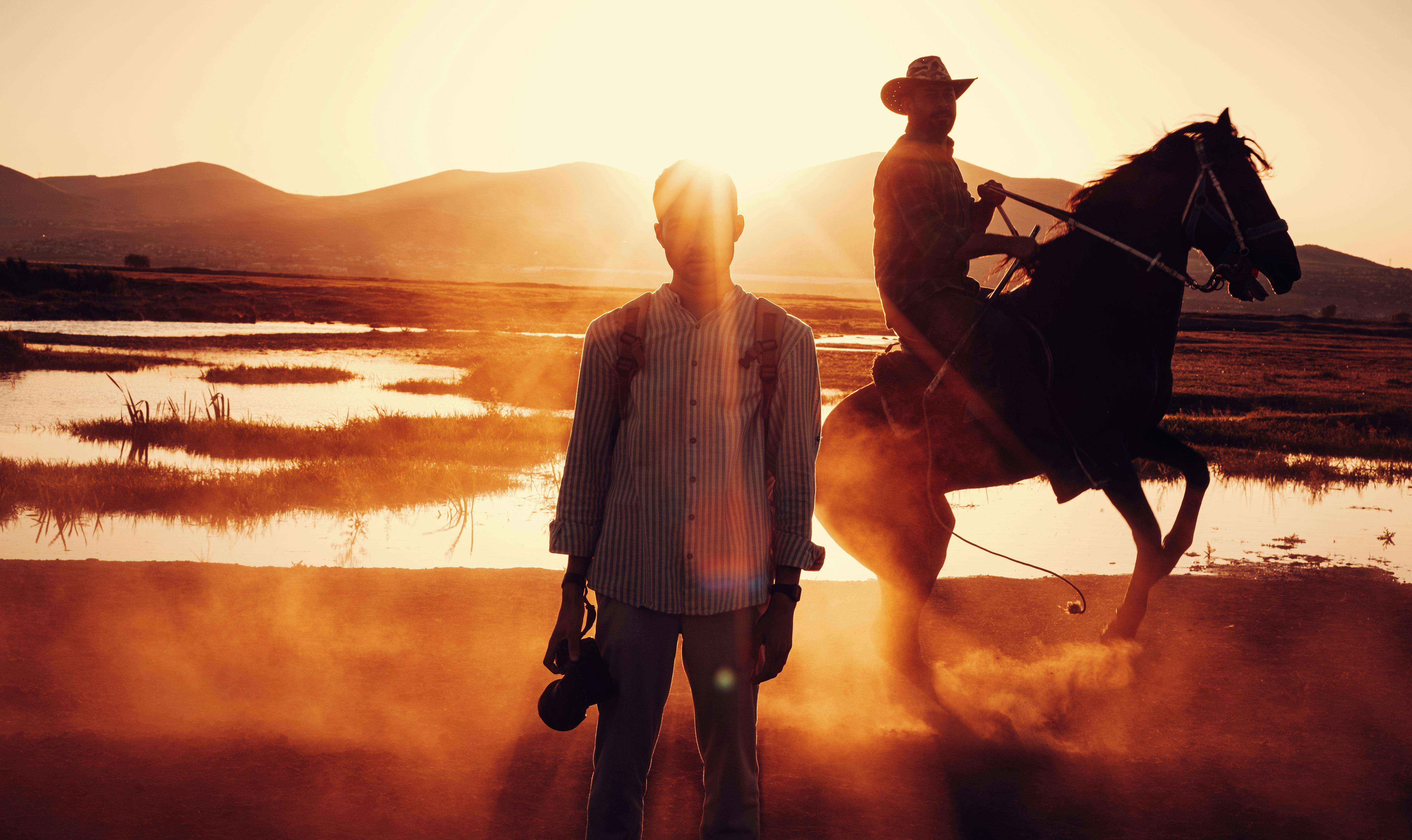 men standing and riding horse in countryside at sunset