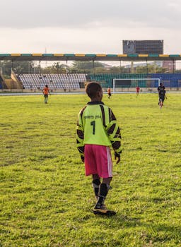 A young soccer player in a bright green jersey standing on a grass field during a match at a stadium.