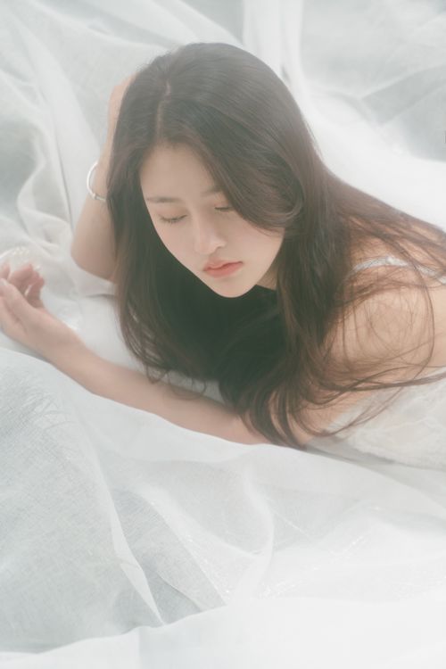 Free A peaceful portrait of an Asian woman lying on a white fabric, captured with a soft and dreamy tone. Stock Photo