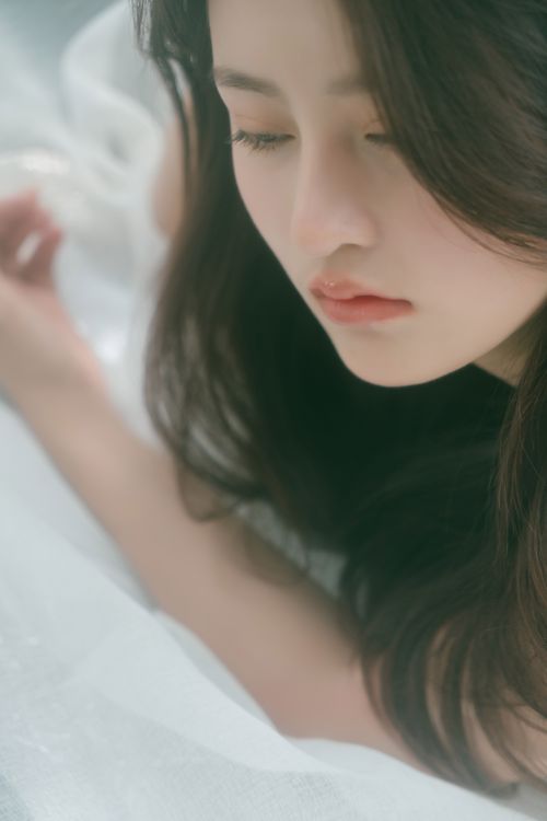 Free Peaceful portrait of a woman lying on white fabric, exuding calmness. Stock Photo