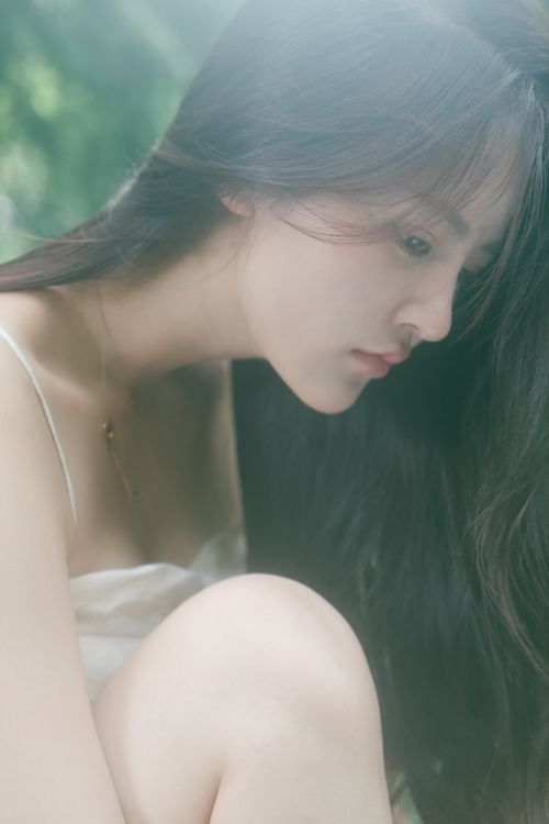 Free A serene side profile of a young woman with long hair sitting outdoors in a garden, captured in a soft, summer light. Stock Photo