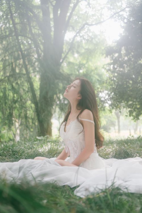Free Peaceful portrait of a woman sitting in a lush green park wearing a white dress. Stock Photo