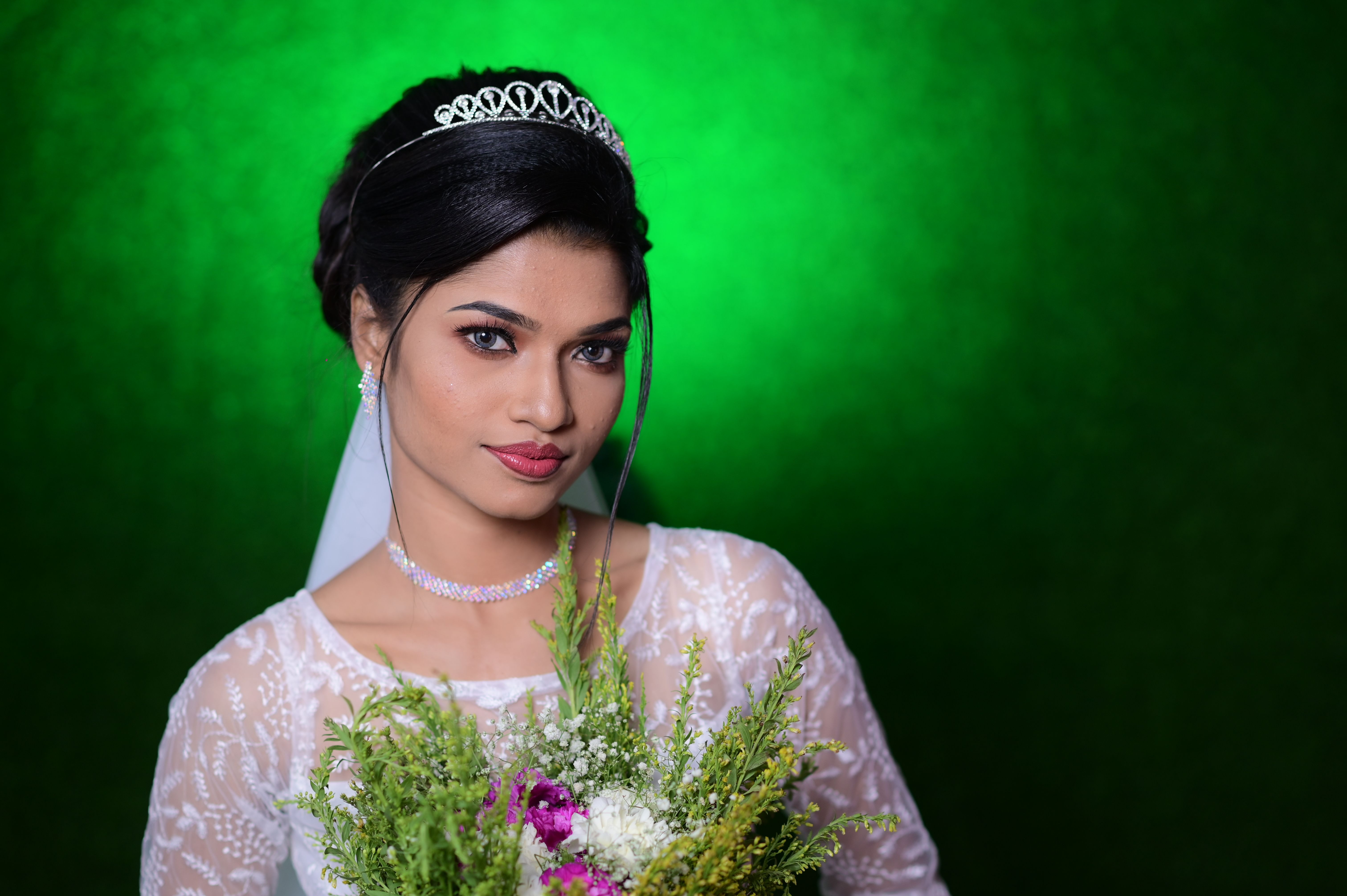 Portrait of a beautiful bride in a lace dress holding a bouquet against a vibrant green background.
