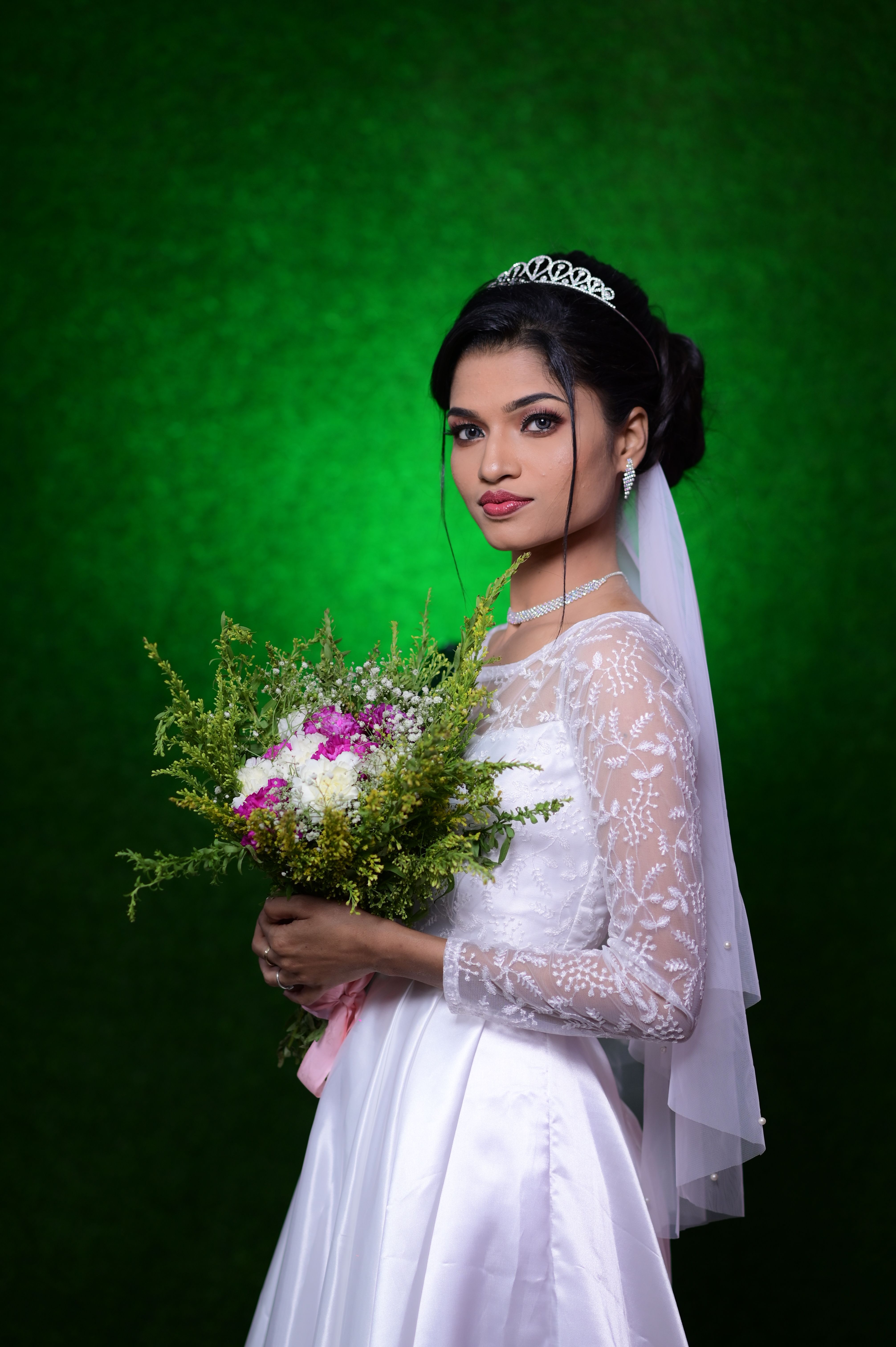 Elegant bride in lace dress holding a colorful bouquet against a vibrant green background.