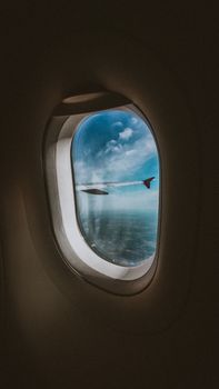 View of airplane wing and clouds through a window, capturing travel and flight essence.