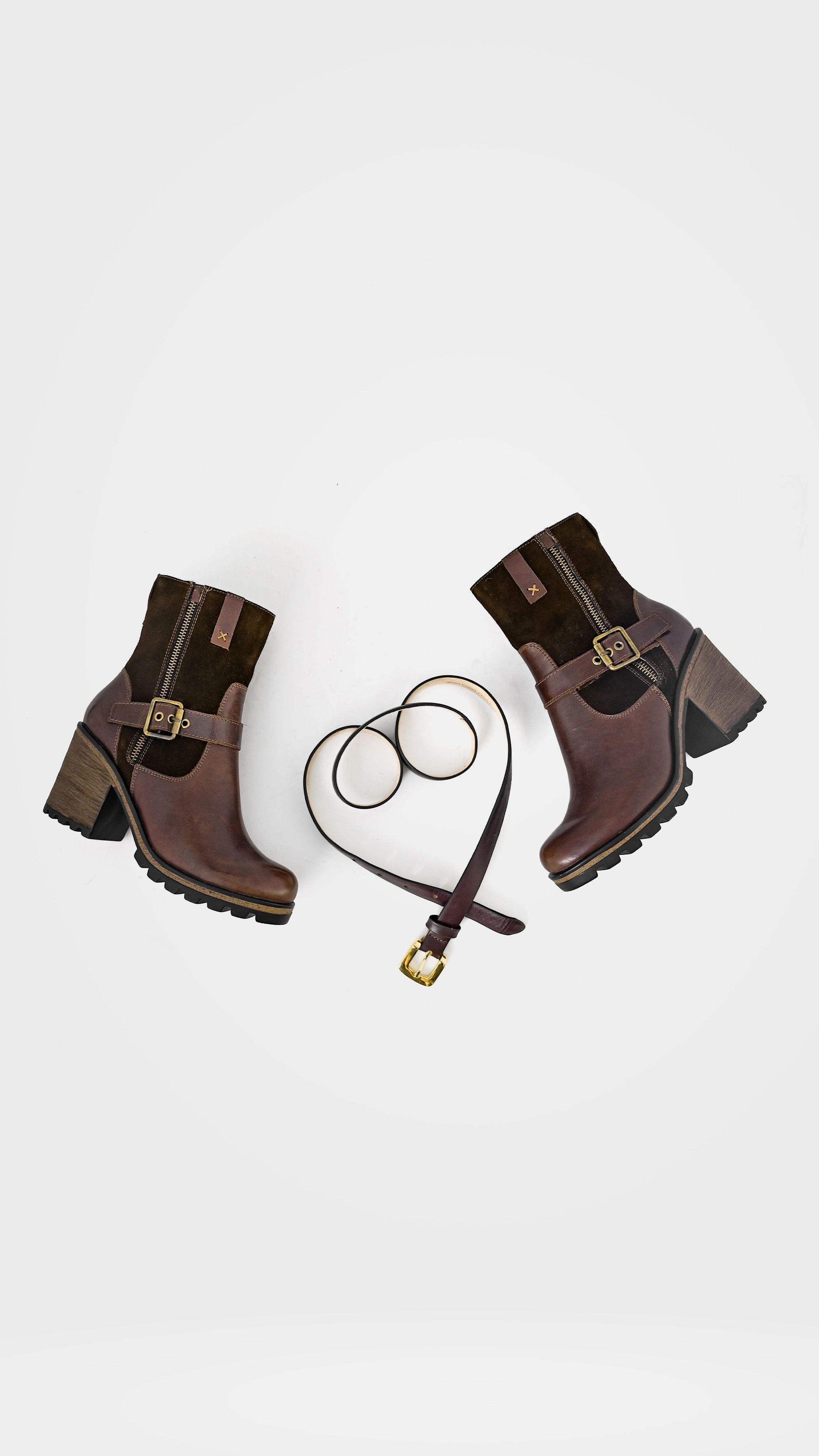 Botas de couro elegantes e cinto dispostos em um estilo flat lay sobre um fundo branco.